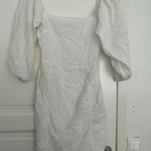Vit kort klänning med puffärmar - Superfin vit kort klänning med puffiga trekvartsärmar och fyrkantig ringning. Klänningen har en lätt skrynklig struktur och är figurnära i modellen. Perfekt för dig som gillar en romantisk och trendig look.etiketen klippte jag av men den är från Nelly