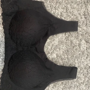 Svart spetsig linnetopp XXL - Svart linnetopp med snygg spetsdetalj över kuporna och sidorna. Toppens material är mjukt och stretchigt, perfekt för en bekväm och stilren look. Bredare axelband och sömlös design gör den extra skön att bära hela dagen.