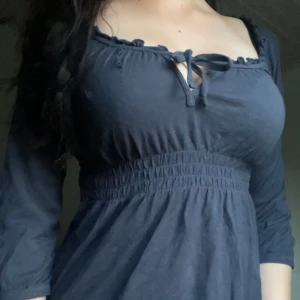 Mörkblå babydoll blus med knyt  - Supersöt mörkblå blus med smockad midja och knyt vid urringningen. Blusen har en trekvartsärm. Perfekt för dig som gillar en feminin och bekväm stil.