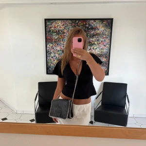 Svart Tiamo väska med kedjedetaljer - Säljer en svart axelväska i skinnimitation med silverfärgade kedjor längs kanterna och som axelrem. Väskan har magnetlås, innerfack med dragkedja och rymligt huvudfack samt 2 små fickor och en ficka på baksidan. Enkel väska som passar till mycket ❣️Märket är Tiamo men den är köpt på Scorett