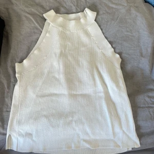 Vit ribbad ärmlös halterneck - Snygg vit polotopp i ribbat material med hög hals och ärmlös design. Perfekt att styla med jeans eller kjol för en clean och fräsch look. Toppens material är mjukt och stretchigt vilket gör den superbekväm.