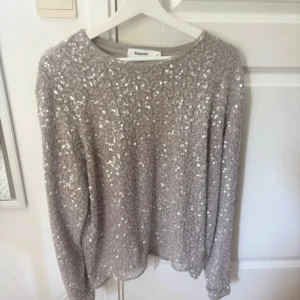 Glittrig beige tröja från Kappahl XL - Superfin beige tröja från Kappahl i storlek XL, täckt med glittriga paljetter som ger ett riktigt snyggt intryck. Tröjan har rund halsringning och långa ärmar, perfekt när du vill sticka ut lite extra.