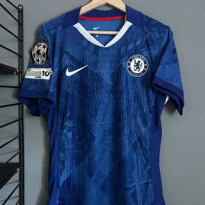 Chelsea FC Palmer 10 matchtröja Nike - Chelsea FCs officiella matchtröja med Palmer 10-tryck på ryggen. Tröjan är blå med vita och röda detaljer, har korta ärmar och klubbmärke på bröstet. Tillverkad i lätt och ventilerande Dri-FIT-material. UEFA Europa League-märke på ärmen helt ny med tagg en replika .