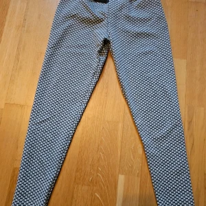 Tränings byxor L - Säljer ett par snygga leggings med svartvitt mönster och hög midja. De är tillverkade i stretchigt material med 92% polyester och 8% spandex, vilket gör dem riktigt bekväma. Perfekta för dig som gillar att sticka ut med coola mönster och vill ha en tight passform, hjälper till att forma rumpan