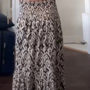 Svartvit långkjol med mönster - Säljer en flowy långkjol med svartvitt grafiskt mönster och smockad midja. Kjolen har en luftig passform och är perfekt för dig som gillar boho-vibes. Materialet känns lätt och skönt mot huden. Perfekt att styla med en enkel topp och sneakers.