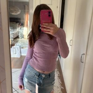 Ljuslila ribbad topp med öppen rygg från NA-KD - Superfin ljuslila ribbad topp från NA-KD med lång ärm och snygg öppen rygg. Figurnära passform och croppad längd, perfekt till jeans eller kjol. Materialet är stretchigt och mjukt, vilket gör den riktigt bekväm och trendig.