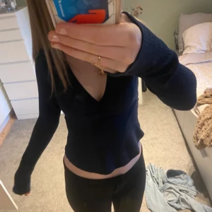 Nelly topp - Snygg marinblå långärmad tröja med djup v-ringning och figurnära passform. Tröjan är croppad och har långa ärmar som sitter skönt. Finns två band där bak som man kan knyta till en roset💞