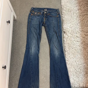 True Religion bootcut jeans blå - Säljer mina true religion jeans som är super low waist och passar perfekt men ganska slitna. de är storlek W24. bak fickan har tappat en knapp och sömmen har gåt upp på vissa ställen. dessutom är jeansen ganska sönder trampade men går fortfarande att använda. 
