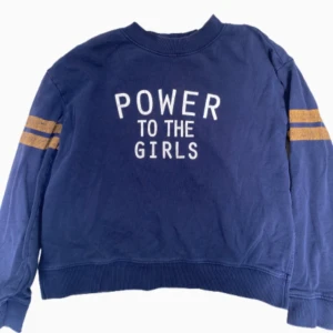 Blå sweatshirt med text och ränder - Blå sweatshirt med vit text 'POWER TO THE GIRLS' på framsidan och två gula ränder på varje ärm. Tröjan  är jätte skön. Hör av dig vid några frågor.💞