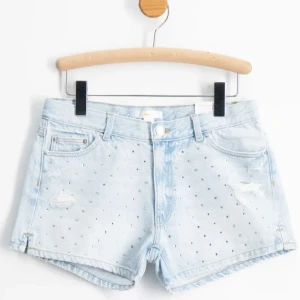 Ljusblå jeansshorts med diamanter från Gina Tricot - Snygga ljusblå jeansshorts från Gina Tricot med silverfärgade diamanter och slitna detaljer framtill. Klassisk femficksmodell med låg midja och råa benslut. Perfekta för sommaren och ger en cool vibe till din outfit. Strl 150 men passar mig perfekt som är 158