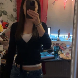 Svart omlottkofta från Gina Tricot - Svart omlottkofta från Gina Tricot med långa ärmar och knytband i midjan. Snygg v-ringning och figurnära passform. Perfekt att styla med jeans eller kjol för en clean look. Nästan aldrig använd, max 2 gånger och det är inga slitningar eller fläckar på den alls. 💕