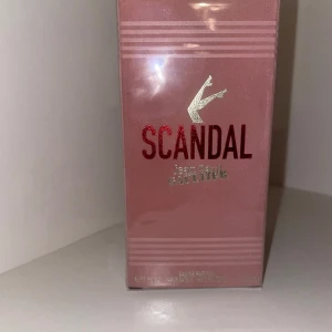 Scandal Jean Paul Gaultier parfym - Scandal från Jean Paul Gaultier är en lyxig parfym i en snygg rosa kartong med metallicdetaljer och röd text. Förpackningen har en ikonisk design med silvriga ben upptill och ger en exklusiv känsla. Perfekt för dig som gillar trendiga och eleganta dofter.