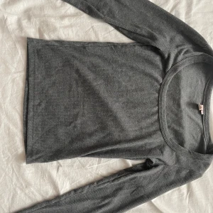 Mörkgrå ribbad långärmad tröja Nelly - Mörkgrå långärmad tröja från Nelly i ribbat material. Tröjan har en rund halsringning och sitter tajt mot kroppen, perfekt att styla med jeans eller kjol. Enkel och stilren design som funkar året runt.