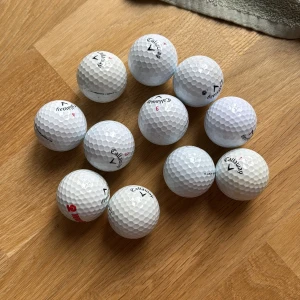 11 st Callaway chrome soft - Bilden visar ett dussin Callaway-golfbollar på ett trägolv. 