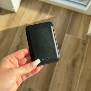 Svart plånbokskorthållare från Holdit - Minimalistisk svart korthållare från Holdit i stilren design. Tillverkad i slätt skinnliknande material med plats för flera kort. Perfekt att fästa på mobilen eller ha i fickan för smidig access till dina viktigaste kort.