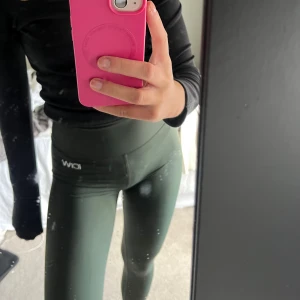 Mörkgröna leggings från ICIW - Snygga mörkgröna leggings från ICIW med hög midja och tight passform. Tillverkade i ett stretchigt och mjukt syntetmaterial som sitter perfekt under träning eller chill. Diskret logga framtill vid höften. Scrunch bak