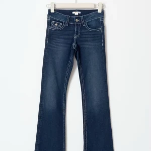 Super low waist bootcut jeans med kontrastsömmar - Snygga mörkblå jeans med bootcut passform och markerade vita kontrastsömmar. Jeansen har klassiska fickor fram och bak med lock och knappdetaljer. Perfekta för dig som gillar en tidlös men trendig look.