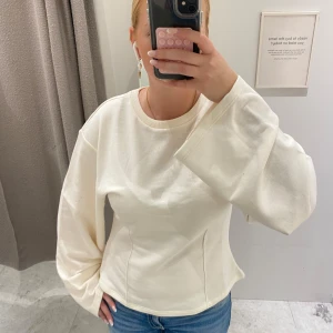 Vit långärmad tröja med vida ärmar - Säljer en vit långärmad tröja med breda och vida ärmar. Tröjan har en rund halsringning och är gjord i mjukt bomullsmaterial. Passformen är normal och den har en clean, minimalistisk look som är enkel att styla med jeans eller kjol.