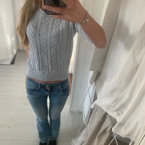 Ljusgrå kabelstickad tröja - Supersöt ljusgrå kabelstickad tröja med rund hals och ribbade muddar. Tröjan har en klassisk stickad look och är lite croppad i modellen. Perfekt till jeans och funkar året runt. Mjuk och skön, passar dig som gillar enkel men snygg stil.