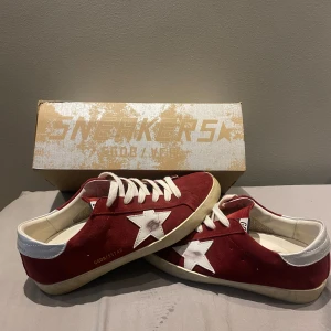 Golden Goose Superstar röda sneakers - Golden Goose Superstar sneakers i röd mocka med vita stjärndetaljer på sidorna och silverfärgade hälpartier. Klassisk låg modell med vita snören och platt sula. Kom med bud, skriv om ni vill ha fler bilder för man kan ju bara lägga upp 5 stycken på plick. Box ingår kan även ta byten 