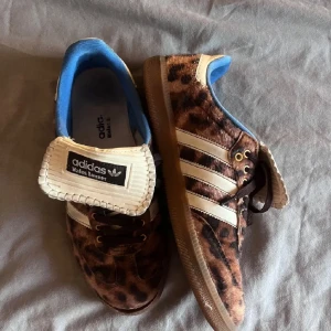 Adidas Wales Bonner leopard sneakers - Unika Adidas Wales Bonner sneakers med leopardmönster i brunt och svart, klassiska vita stripes och blå insida. Ovandel i pälsliknande material, gummisula och detaljer i beige. Perfekta för dig som vill sticka ut med coola och trendiga skor.