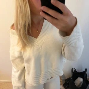 Vit stickad v-ringad tröja - Superfin vit stickad tröja med bred v-ringning och ribbade kanter. Modellen är lite croppad och har en loose passform med långa ärmar. Perfekt att slänga på sig för en chill och stilren look.