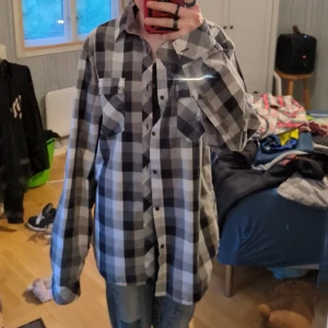 Rutig skjorta från JC i svart och grått - (vill tillägga att en knapp på höger arm saknas) Säljer en oversized rutig skjorta från JC i svart, grått och vitt. Skjortan har klassisk krage, knappar framtill och två bröstfickor med lock. Perfekt att bära öppen över en t-shirt eller stängd för en chill look.