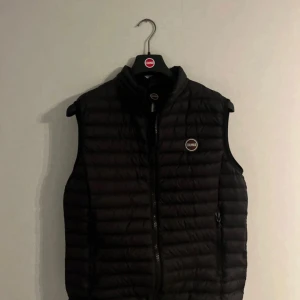 Svart dunväst från Colmar - Snygg svart dunväst från Colmar med quiltad design och dragkedja framtill. Västen har två sidofickor med dragkedja och rundad krage. Colmar-logga på bröstet och nedtill. Perfekt att slänga över en hoodie för extra värme.