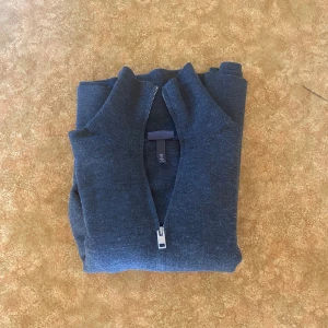 Mörkgrå stickad kofta  - Säljer en mörkgrå stickad kofta med hel dragkedja och hög krage. Koftan är långärmad och har en clean, enkel look som passar perfekt till jeans. Materialet är mjukt och stretchigt för en skön passform. 