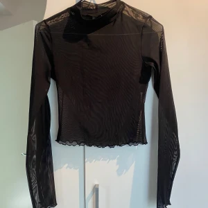 Svart mesh polotopp med lång ärm - Säljer en svart mesh långärmad topp. Den har vågig kant nedtill och är perfekt för att styla lager på lager. Enkel men ändå riktigt snygg.