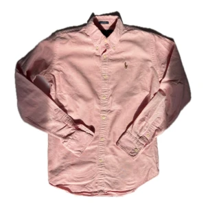 Rosa skjorta från Ralph Lauren - Snygg rosa skjorta från Ralph Lauren i slim fit-modell. Skjortan är i bomull, har klassisk krage med knappar och det ikoniska broderade logotypen på bröstet. Långärmad och perfekt för dig som gillar stilrena plagg med en fräsch färg.
