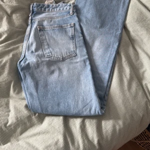 Ljusblå jeans från Zara, storlek 36 - Säljer ett par klassiska ljusblå jeans från Zara i storlek 36. De har raka ben, fem fickor och medelhög midja. Jeansen är i mjukt bomullsdenim och har snygga detaljer med silverfärgade knappar och bälteshällor.