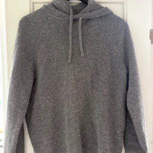 Grå kashmir hoodie från J.Crew - Säljer en grå hoodie från J.Crew i 100% kashmir. Tröjan har en mjuk stickad struktur, huva med snörning och långa ärmar. Perfekt för dig som gillar chill och stilren look. Passar dig som vill ha något extra skönt och snyggt i garderoben.