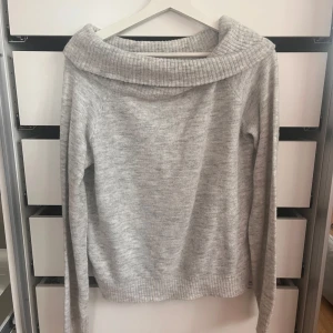 Ljusgrå off shoulder tröja från H&M - Säljer en ljusgrå off shoulder stickad tröja från H&M. Tröjan har långärmade ärmar och är mjuk och skön, perfekt för kyliga dagar. Enkel och stilren design som funkar till många olika outfits.