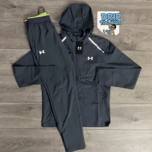 Svart träningsset från Under Armour - Snyggt svart träningsset från Under Armour med jacka och byxor. Jackan har huva, dragkedja och reflekterande detaljer vid axlarna. Båda delarna har Under Armour-logga framtill. Perfekt för dig som vill ha en sportig look.