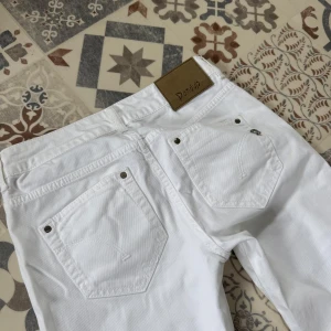 Vita jeansbyxor från Dondup - Snygga vita jeansbyxor från Dondup med klassisk femficksdesign och silverfärgade nitar. Byxorna har rak passform och är tillverkade i bomullstyg. Perfekta för dig som vill ha en clean och fräsch look. Dem har någorlunda små fickor. Storlek 30!