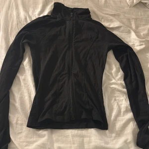 Svart zip-kofta från Gina Tricot XS - Svart tajt tränings kofta från Gina Tricot i storlek XS. Modellen är figurnära med hel dragkedja framtill och hög krage. Långärmad och tillverkad i mjukt material, perfekt för lager-på-lager. Enkel och stilren design som funkar till allt.