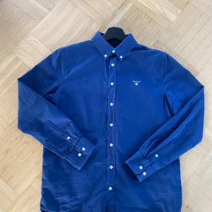 Marinblå bomullsskjorta från Gant - Snygg marinblå skjorta från Gant i mjuk bomull. Klassisk button-down krage, vita knappar och broderad logga på bröstet. Långärmad modell med normal passform, perfekt till jeans eller chinos.