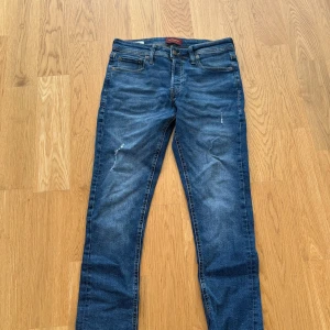 Blå jeans från Jack & Jones, storlek 28/30 - Snygga blå jeans från Jack & Jones med klassisk femficksdesign och bruna sömmar. Modellen har en rak passform och normal midja. Materialet är slitstarkt denim i bomull. Perfekt för dig som gillar en enkel och tidlös stil. Köpta för 799kr på Jack & Jones men mitt pris 199kr