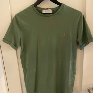 Grön t-shirt från Les Deux - Snygg grön t-shirt från Les Deux med liten gul broderad logga på bröstet. Klassisk rund halsringning och uppvikta ärmslut ger en clean och stilren look. Perfekt till jeans eller shorts för en chill vibe. Använd en gång säljer den pga passar inte i färgen enligt mig själv. Ny kostar 449kr. Tveka inte på att skriva om ni har frågor!