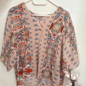 Mönstrad blus med knappar - Säljer en luftig blus med vackert paisleymönster i beige, blått, rött och grönt. Blusen har v-ringning, knappar framtill och vida trekvartsärmar. Perfekt för dig som gillar bohemisk stil och färgglada detaljer.