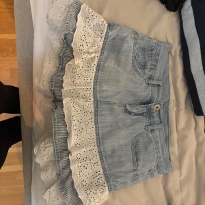 Ljusblå jeanskjol med volang och spets - Supersöt ljusblå jeanskjol med volanger i vitt och broderad spets. Kjolen har klassiska jeansdetaljer som fickor och bälteshällor, och volangerna ger en romantisk och lekfull vibe. Perfekt för dig som vill sticka ut med en unik och feminin stil. kjolen är i storlek 164 men jag som är en xs/s kan ha den utan problem!!