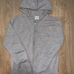 Beige cashmere hoodie från John Henric - Mjuk och lyxig hoodie i beige från John Henric, tillverkad i 100% cashmere. Tröjan har huva, dragkedja framtill och långa ärmar. Perfekt för dig som gillar stilrena och bekväma plagg med exklusiv känsla.