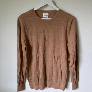 Beige merinoulltröja från A Day's March - Säljer en stilren beige tröja från A Day's March i 100% merinoull. Tröjan har rund hals, långärmad design och ribbade muddar vid ärmslut och nederkant. Perfekt för dig som gillar klassisk och enkel look med premiumkänsla. 1F2