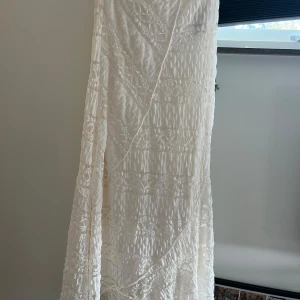 Vit lång spetskjol XS - Säljer en superfin lång kjol från GinaTricot i offwhite med spetsdetaljer och omlott-design. Kjolen har ett romantiskt uttryck med genombrutet spetsmönster och mjukt fallande tyg. Perfekt för dig som gillar boho-vibe och vill sticka ut med en elegant look. Den är helt oanvänd och i nyskick. Orginalpris ligger på 400kr