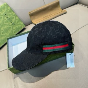 Svart Gucci keps med GG-mönster - Snygg svart keps från Gucci med klassiskt GG-mönster över hela ytan och en ikonisk grön-röd rand på sidan. Justerbar rem baktill med Gucci-logga. Materialet är bomull och polyester, perfekt för dig som vill ha en lyxig streetstyle-look.