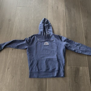 Blå hoodie från Tommy Hilfiger M - Snygg marinblå hoodie från Tommy Hilfiger med broderad logga på bröstet. Tröjan har huva med snörning, känguruficka och långa ärmar. Perfekt för en chill och stilren look.