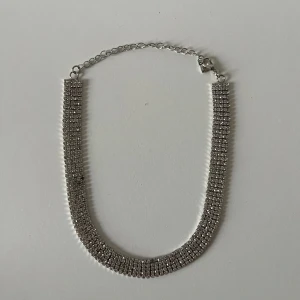 Glittrigt silverhalsband - Snyggt halsband i silverfärg med flera rader glittrande stenar som ger en lyxig känsla. Kedjan har justerbar längd och ett smidigt spänne. .