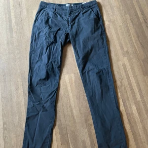 Mörkblå chinos från Dondup, stl 32 - Snygga mörkblå chinos från Dondup i storlek 32. Byxorna har klassisk rak passform, sidofickor fram och två bakfickor med knapp. Tillverkade i ett mjukt bomullsmaterial med diskret struktur och metallogo bak. Perfekta för en clean och stilren look.