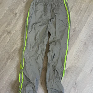 Reflekterande byxor med neonränder - Säljer ett par gråa byxor med reflekterande effekt. Byxorna har elastisk midja och neongröna ränder längs sidorna. Väldigt små i storleken, står L men snarare S eller en liten M
